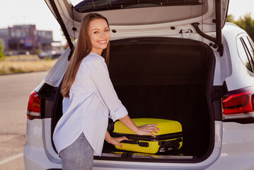 Photo portrait smiling girl put baggage in the car going to airport