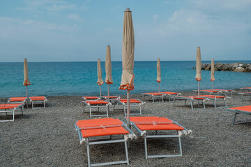 Orange beach chairs and umbrellas on the pebble beach across beautiful blue seacoast till the horizon.  Summer vacation. Hotel beach. Sestri Levante, Liguria, Italy