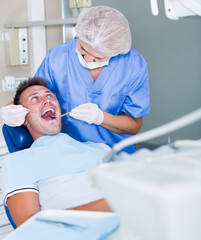 Fototapeta premium Professional dentist examining and performing treatment to young man