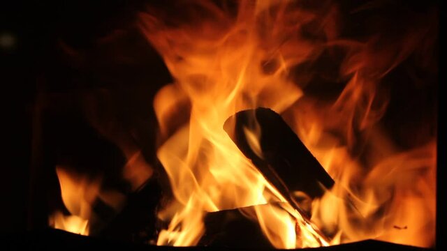 Firewood in a blazing fire. Close-up view of a sparkling flame in a stove, fireplace. Orange-yellow tongues of fire in fireplace at evening, night time. Abstract video footage. Cozy home atmosphere.