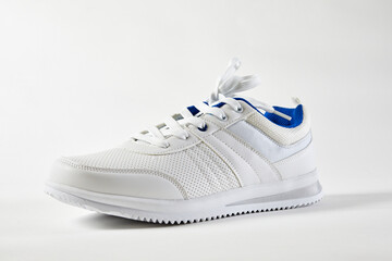 White sports sneakers with shoelace on a white wall background. Man sneakers for fitness. White sneaker with leather accents.