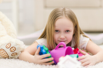 Cropped photo of blond girl laying on the floor with toys.