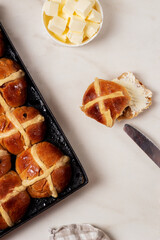 Fresh homemade Traditional Easter treats hot Cross Buns with raisins, served with butter and knife on marble bench top