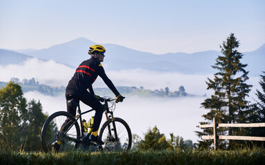 Silhouette of man cyclist in cycling suit riding bike on grassy hill. Male bicyclist enjoying the...