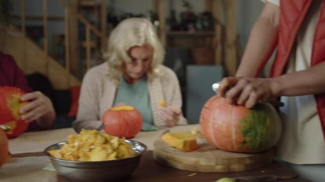 Family sitting at the table and taking out the pulp from the pumpkin and carving the lamps for Halloween