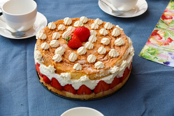 RunderGeburtstagstorte mit Erdbeeren und kleinen Sahnehäubchen auf gedecktem Tisch