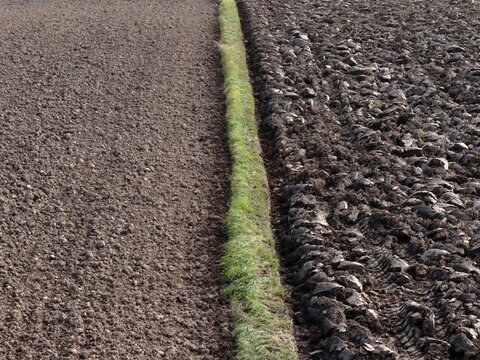 Aerial view of contrasting plowed and unplowed agricultural fields separated by a narrow grassy strip. Soil structure and farming patterns in rural landscape