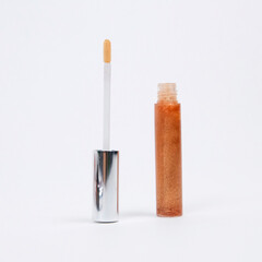 A minimalistic peach glitter colour lip gloss tube with silver wand in front of white background.