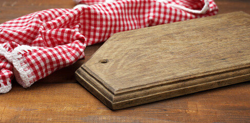old wooden cutting board and folded red and white cotton kitchen napkin on a wooden brown...
