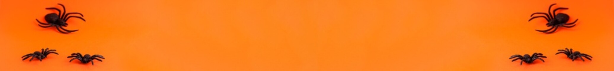 Flat lay banner of black horror spiders of different sizes directions on orange on the left and right backdrop with copy space. Halloween decoration spooky background concept for holidays