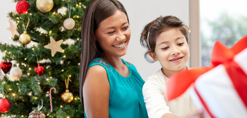 winter holidays, family and people concept - happy mother and daughter with gift at home over christmas tree background