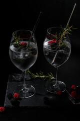 two gin tonc with berry and rosemary on a balck background
