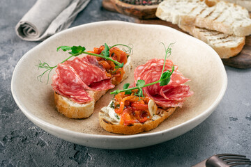 toasted bread with salami and tomatoes and herbs on a plate on the kitchen table. Open sandwiches with Italian salami