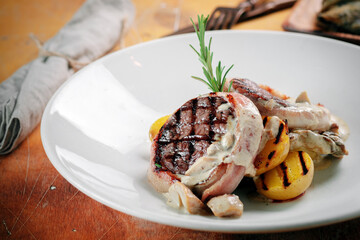 Grilled beef steak baked with bacon with mushroom sauce and potatoes, served on a white plate.