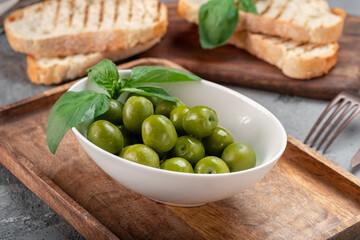 Large green ripe olives in a white bowl on a wooden table. Pickled olives with toast for breakfast