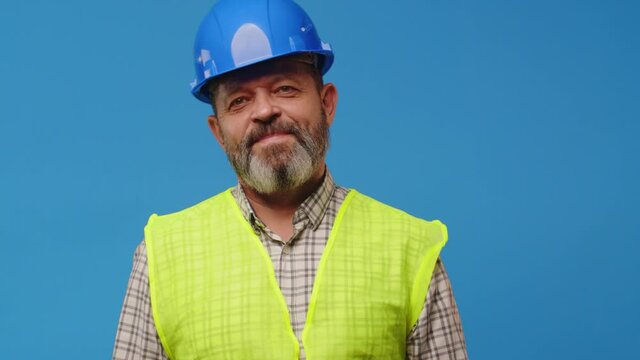 Smiling senior man builder in vest and hardhat against blue background