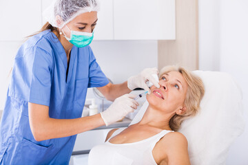 Mature female client receiving cosmetic injection from professional cosmetician