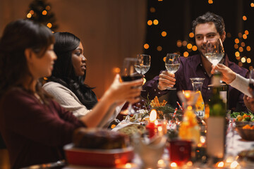 holidays, party and celebration concept - multiethnic group of happy friends having christmas dinner at home and drinking wine