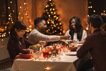 holidays, party and celebration concept - multiethnic group of happy friends having christmas dinner at home
