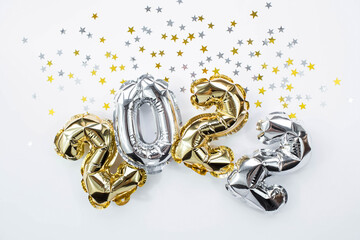 Banner. Happy New Year holiday. Balloons made of gold and silver foil with the number 2022 and confetti in the shape of stars on a white background. Flat lay.
