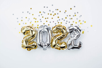 Banner. Happy New Year holiday. Balloons made of gold and silver foil with the number 2022 and confetti in the shape of stars on a white background. Flat lay.