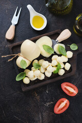 Above view of scamorza cheese with green basil leaves and olive oil, vertical shot on a dark-brown stone background