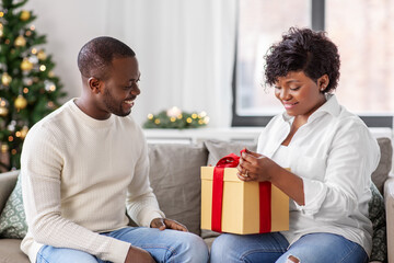 holidays, celebration and people concept - happy african american couple with christmas gift at home