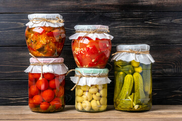 Homemade pickled cherry tomatoes, cucumbers, champignons, garlic, eggplant, red peppers in jars on wooden shelf Homemade canned and fermented foods concept Seasonal product