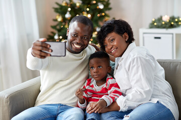 family, winter holidays and people concept - happy african american mother, father and little son taking selfie at home on christmas