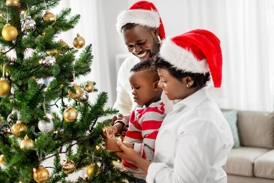 family, winter holidays and people concept - happy african american mother, father and baby son decorating christmas tree at home on