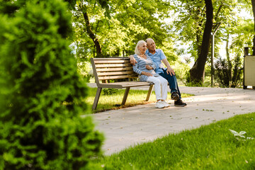 White senior couple hugging and smiling while sitting on bench