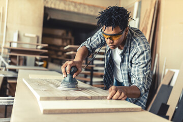 Young carpenter working in his workshop. He's finishing the wooden plank with sand paper.		