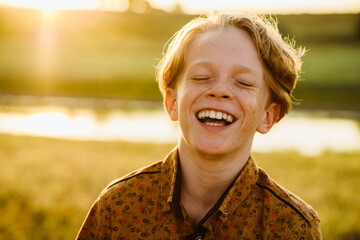 White ginger boy laughing at camera on summer field