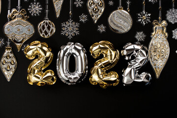 Banner. Happy New Year and Merry Christmas. Balloons made of gold and silver foil with the number 2022, snowflakes, garland and Christmas tree balls on a black background. Flat lay.