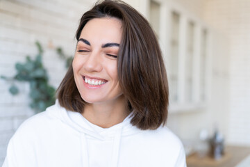 Close up portrait of laughing woman in cozy white hoodie at home in kitchen