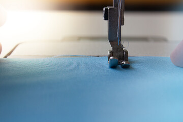 Part of a sewing machine. Sewing machine needle and blue fabric. The concept of small business development.