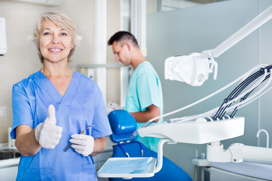 Positive female dentist smiling with thumb up in a dental office