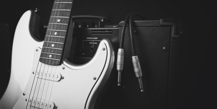 Black guitar amplifier with jack cable and silver electric guitar isolated on white background.