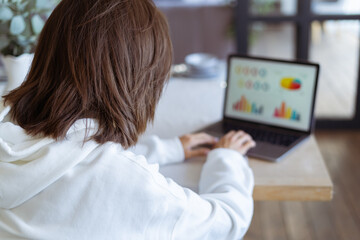 Fototapeta na wymiar Young woman at home in the kitchen in a white hoodie with a laptop, advisor financial business analytics woman with data dashboard graphs