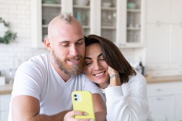 Young couple husband with wife at home in the kitchen, happy chatting by video call, taking selfie on mobile phone