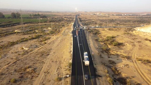 Tracking from above for a heavy truck driving to the crossroad with a new traffic light in Negev desert at sunrise