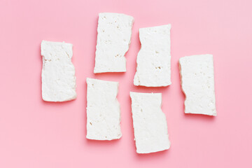 Cut pieces of tofu on pink background close-up top view.