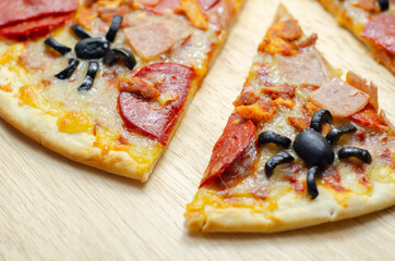 Meat feast pizza on thin dough decorated with black olives in the shape of spiders, food for Halloween party