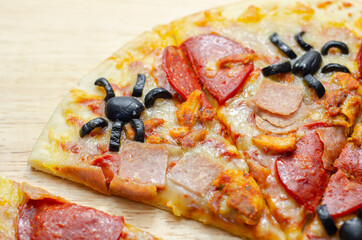 Meat feast pizza on thin dough decorated with black olives in the shape of spiders, food for Halloween party
