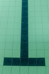 Dark tiles of a pool in the shape of a T that identifies the arrival in a pool, this one has dirty water and the bottom too, the color is greenish
