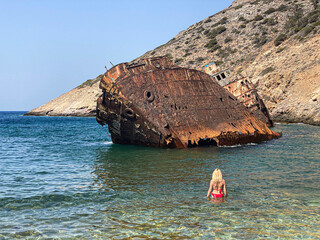 Back view on a woman wearing a red bikini looking at Shipwreck Olympia boat in Amorgos island during summer holidays, Cyclades, Greece. Travel background - obrazy, fototapety, plakaty