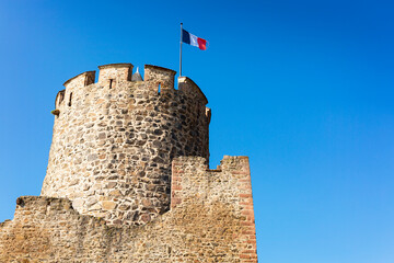 Old castle tower with clear blue sky and French flag, Kaysersberg, Alsace, France