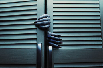 Horror blue toned cupboard or closet doors with scary female monster hands opening it. - obrazy, fototapety, plakaty