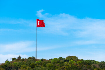 Turkish flag waving in the blue sky, wooded hill. Flagpole.