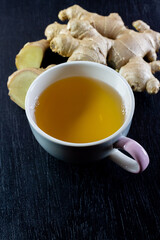 Ginger tea in ceramic cup and fresh ginger with sliced on black wooden background. The scientific name is zingiber officinale. Herbs for health care concept.